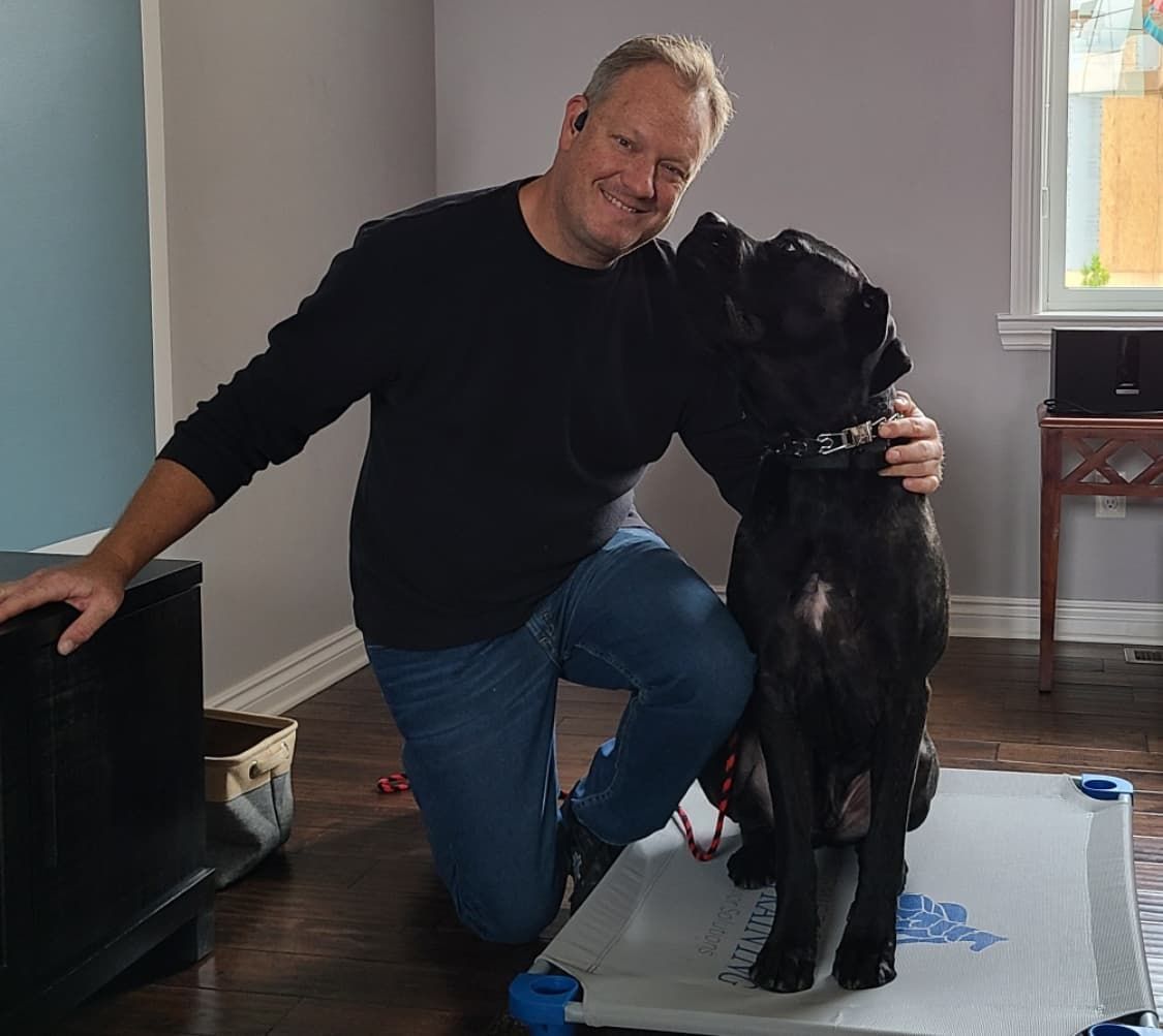 A man is kneeling down next to a black dog