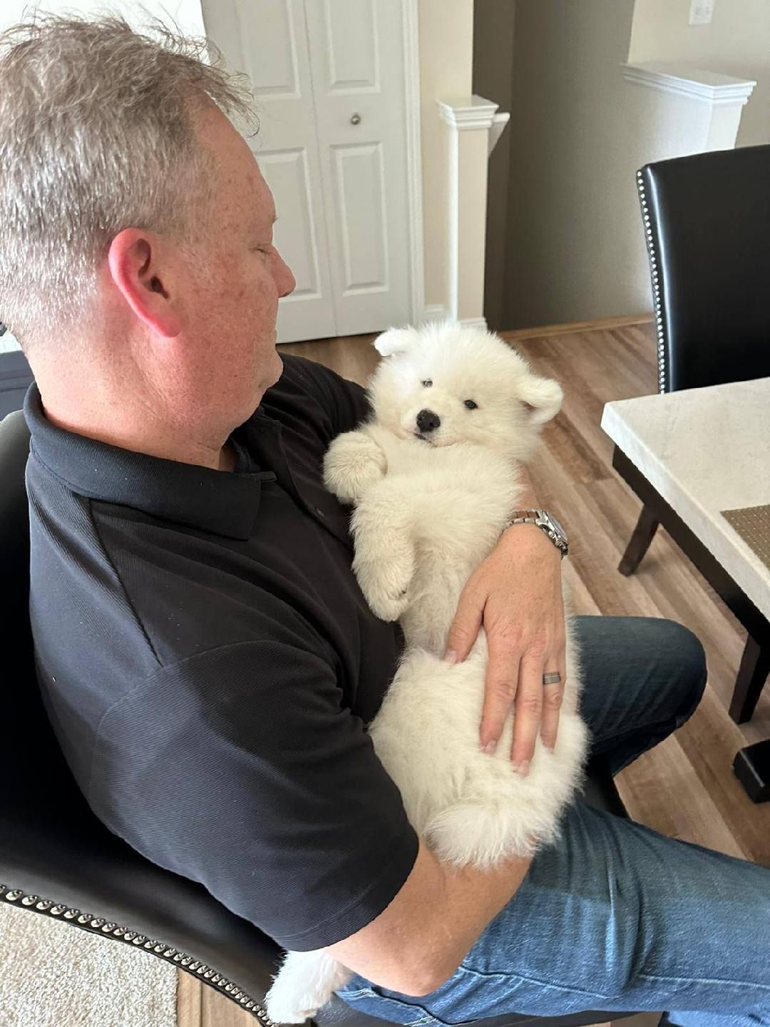 A man is holding a small white puppy in his lap