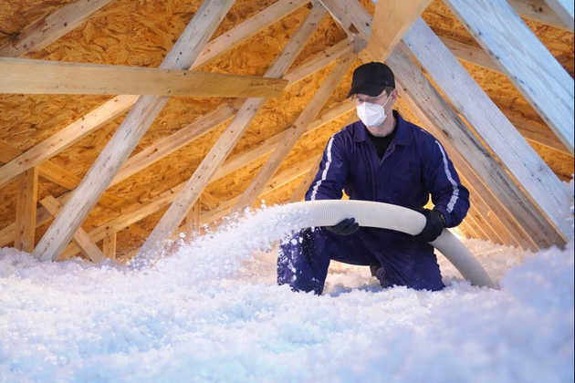 Insulation being blown into an attic from a white hose, covering the floor. Insulation being blown into an attic from a white hose, covering the floor.