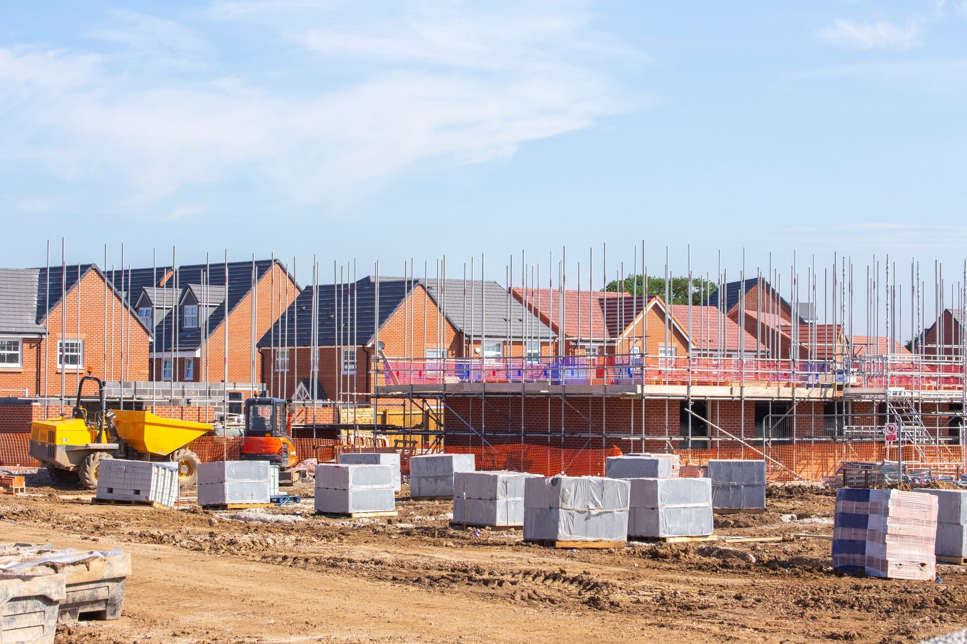 Construction site with brick houses under construction and stacked building materials under a blue sky