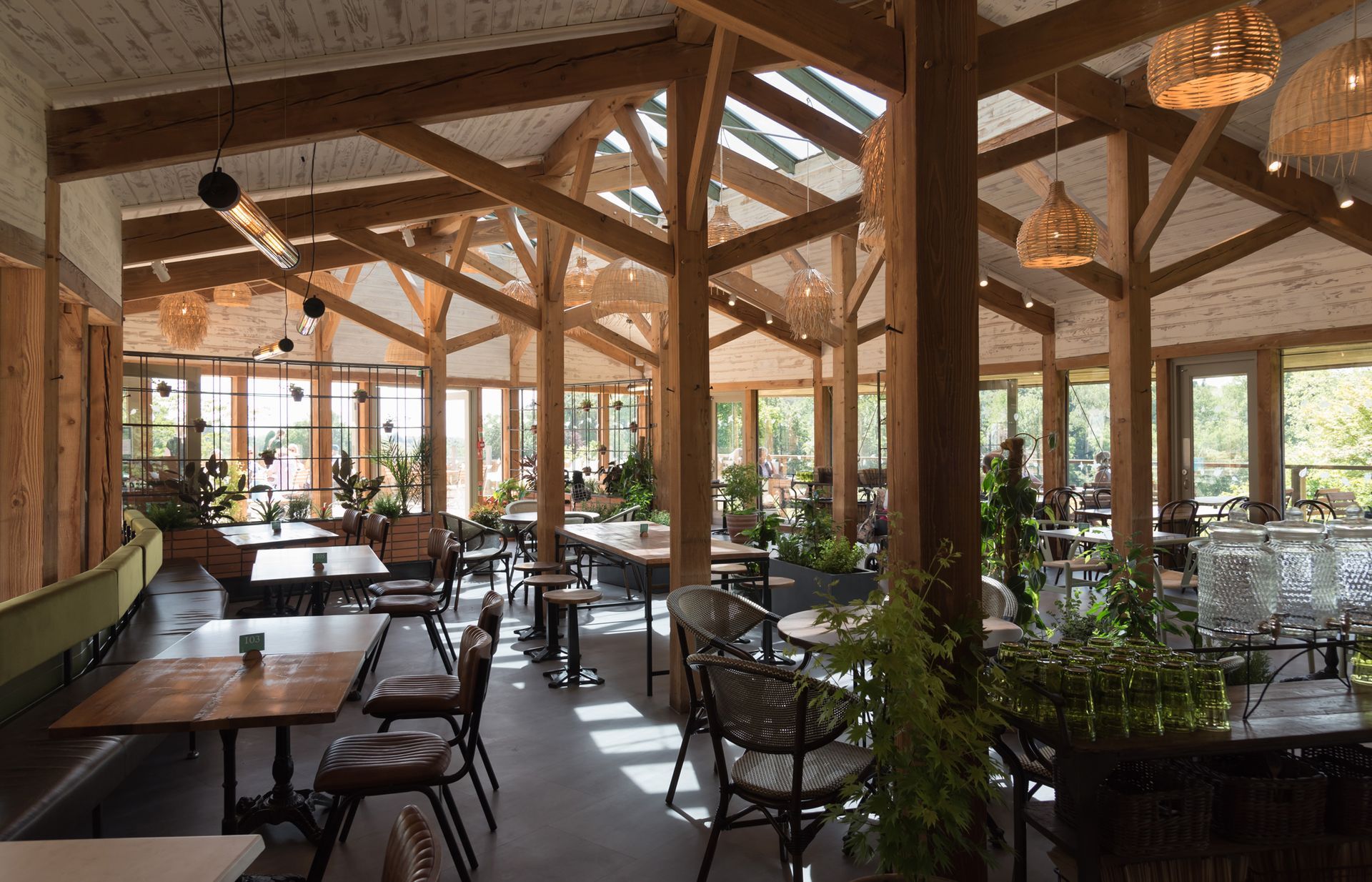 Open-air restaurant with wooden beams, tables, chairs, and potted plants in warm sunlight