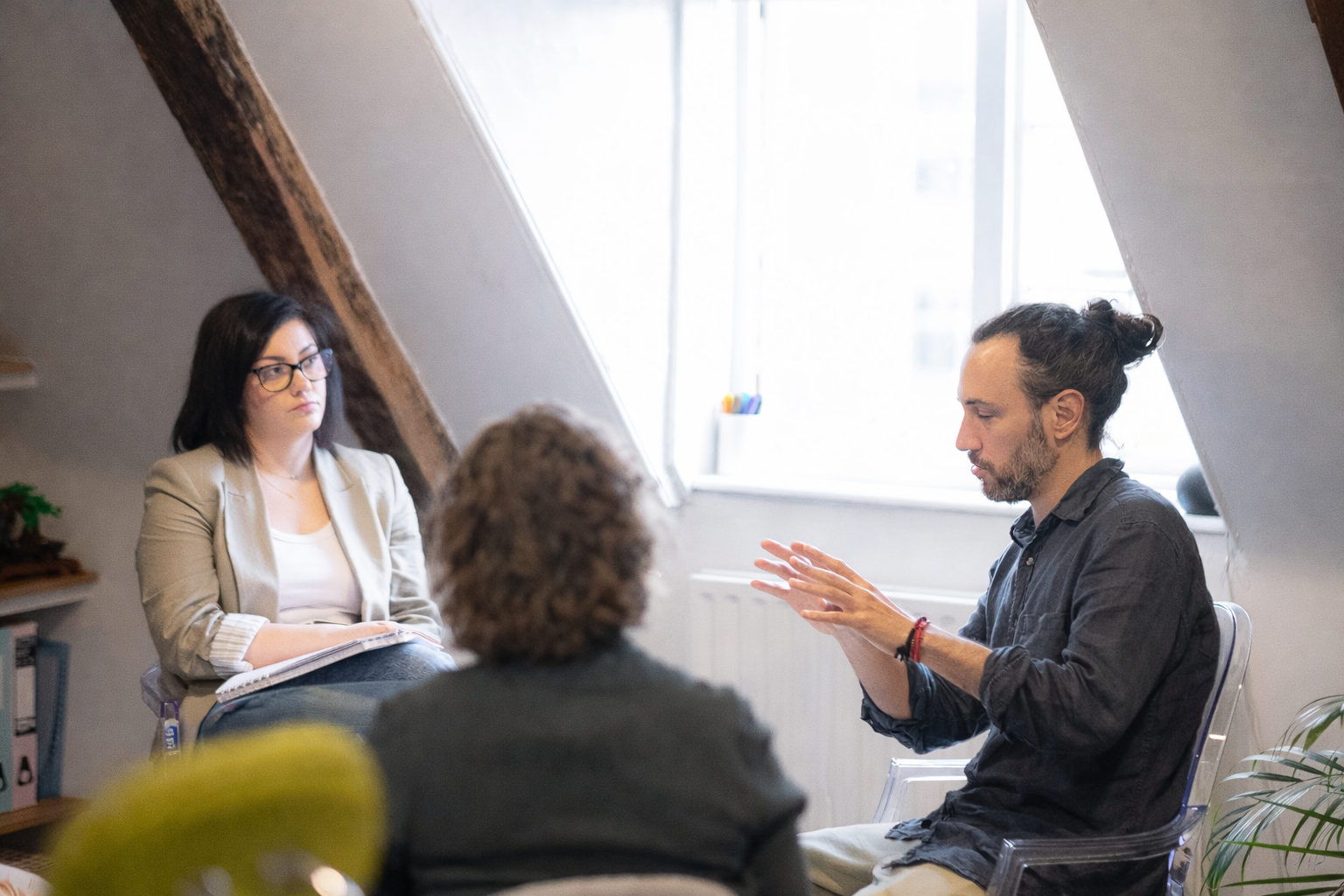 Three people in a bright office meeting, discussing seated around a table