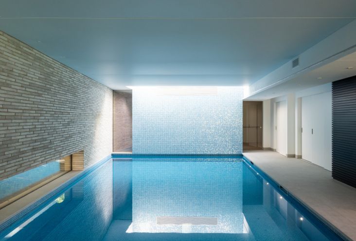 Indoor lap pool with blue water, white tiled walls, and bright skylight reflection