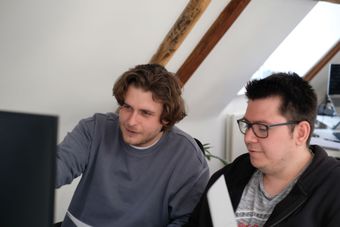 Two people working at a computer in a bright office with slanted wooden beams