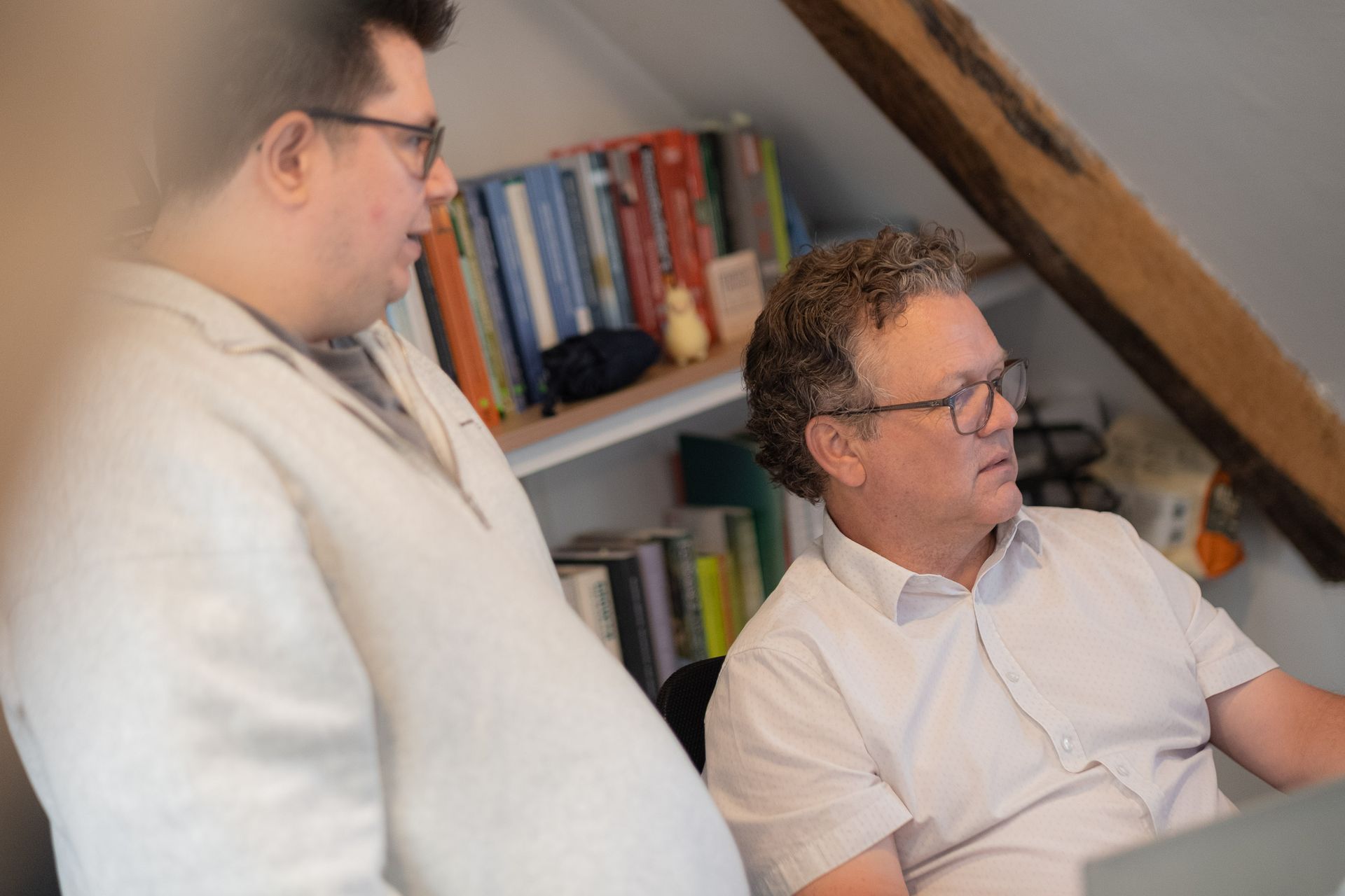 Two people in white shirts talking in a room with bookshelves