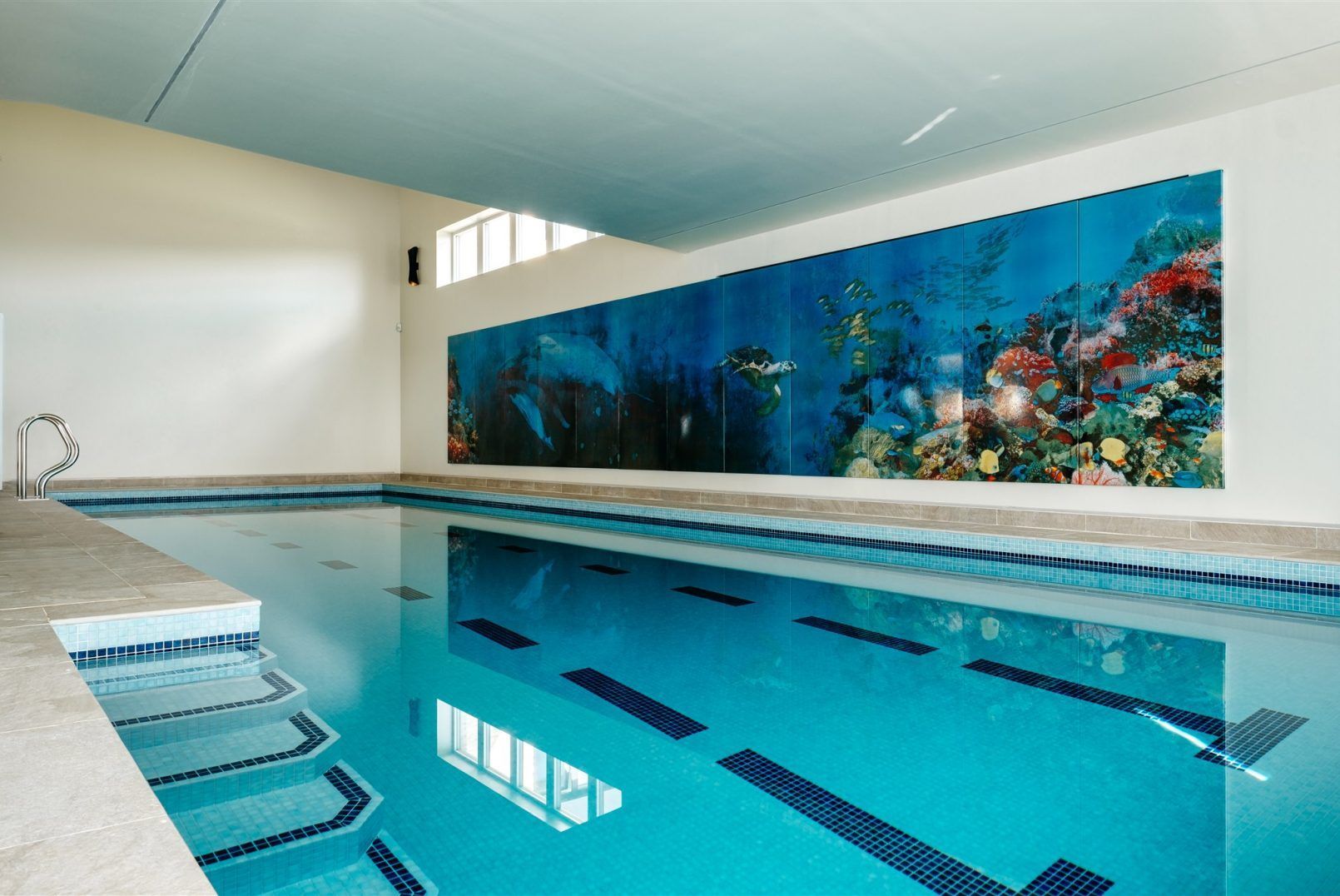 Indoor swimming pool with turquoise water and a large colorful underwater mural on the wall
