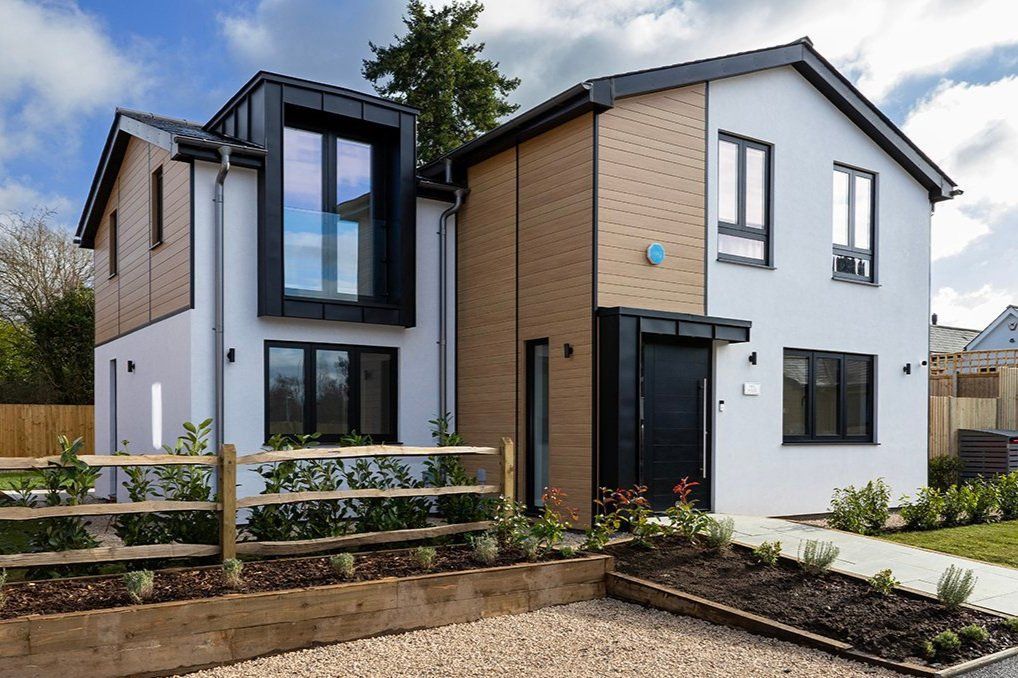 Modern two-story house with white and brick exterior, black-framed windows, and a landscaped front garden