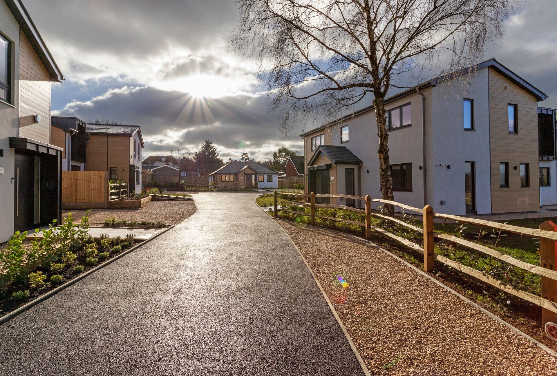 Sunny residential street with modern houses and a wet path under cloudy skies