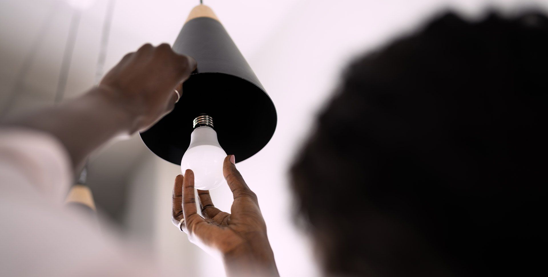 Hands replacing a bulb in a black ceiling light fixture