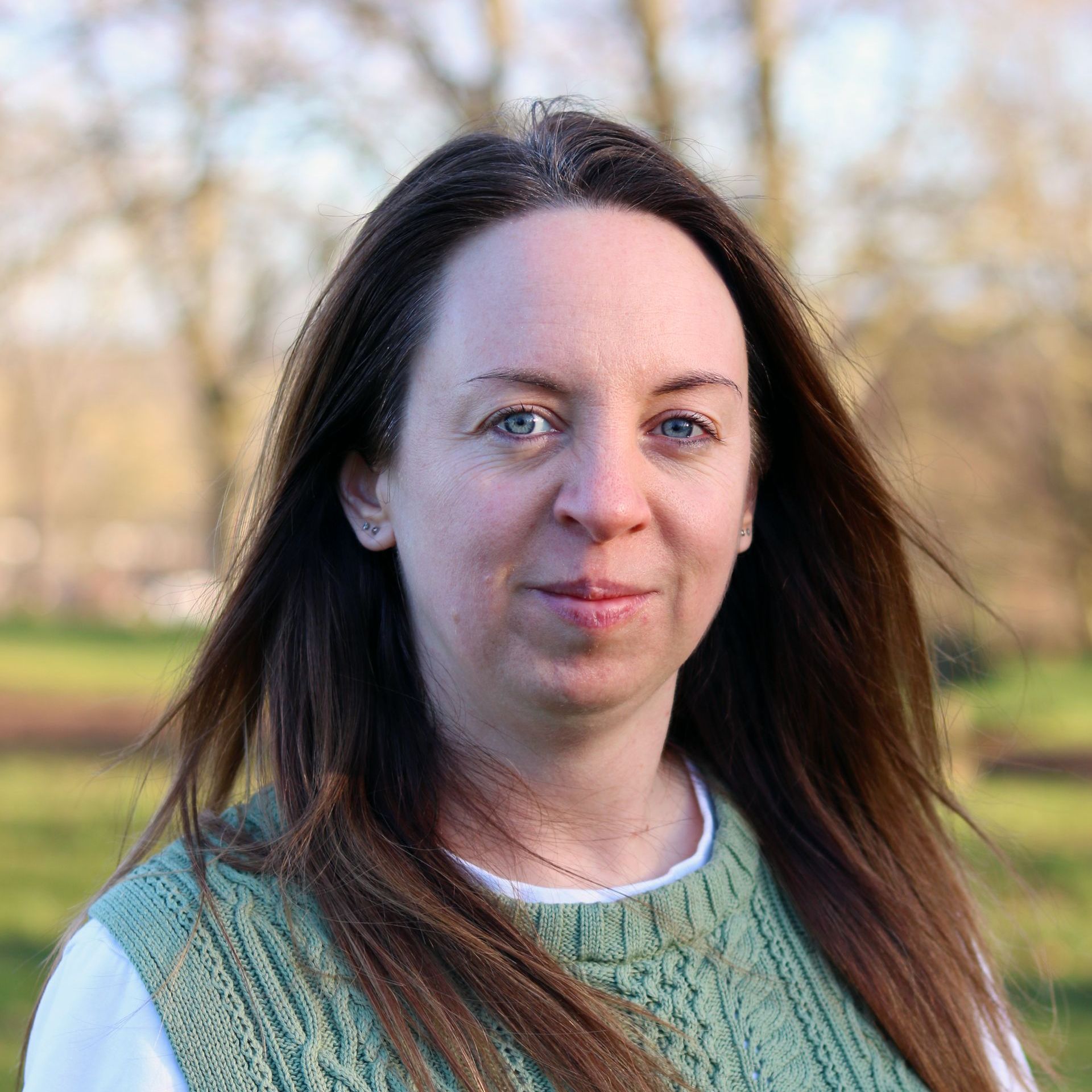 Portrait of a woman outdoors with long dark hair, wearing a green sweater in a park