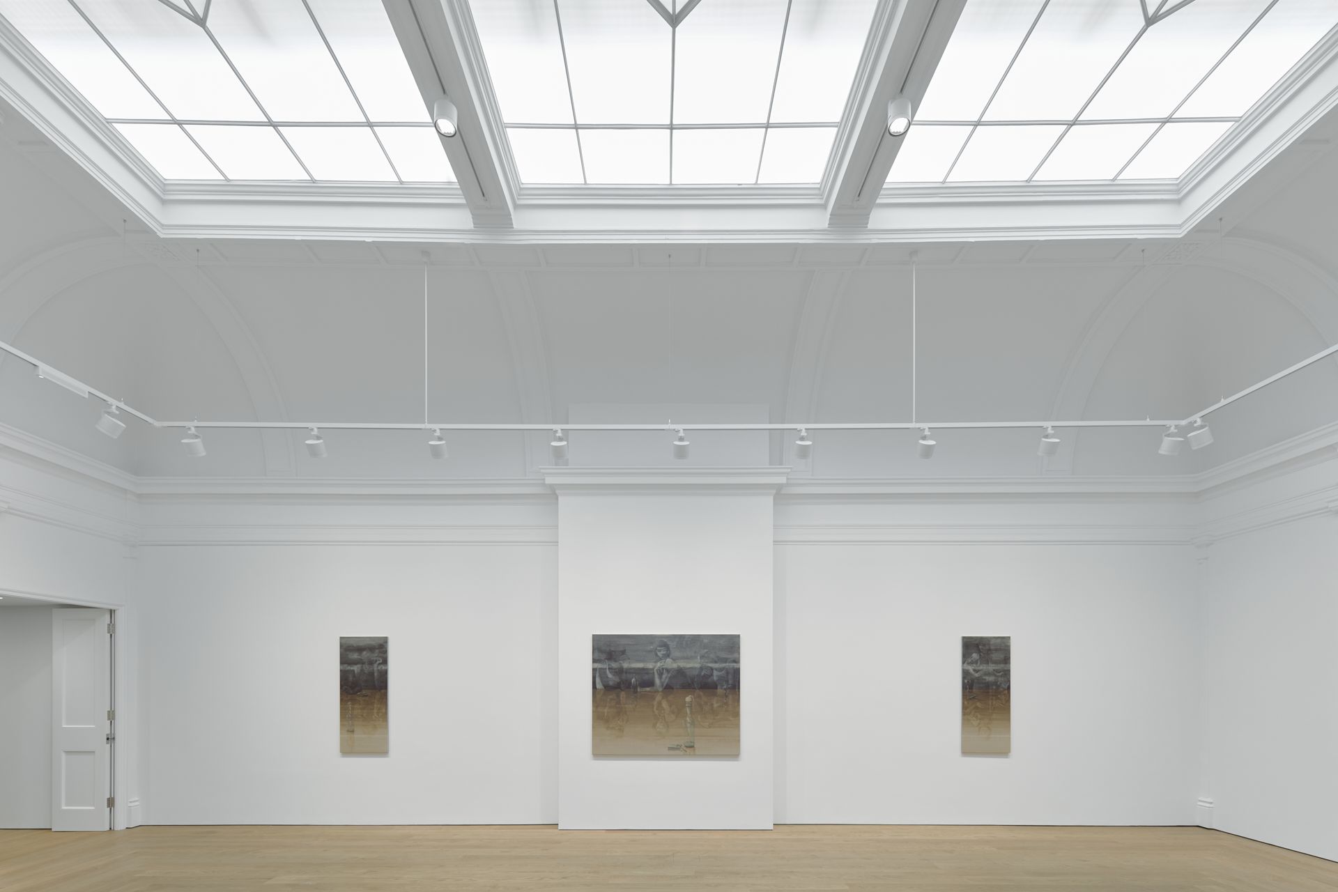 Minimal art gallery with three framed landscape paintings on white walls under skylights.