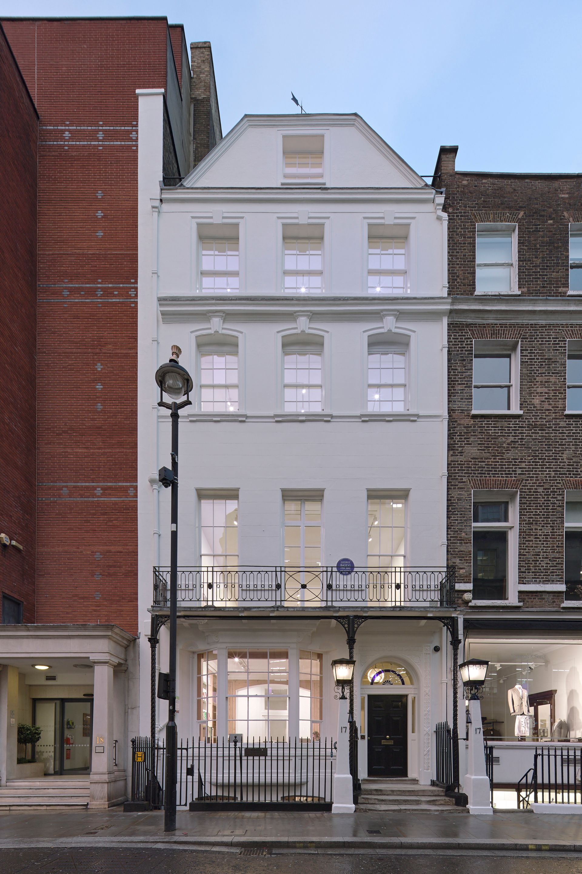 White four-story townhouse with lit storefront windows on a city street at dusk