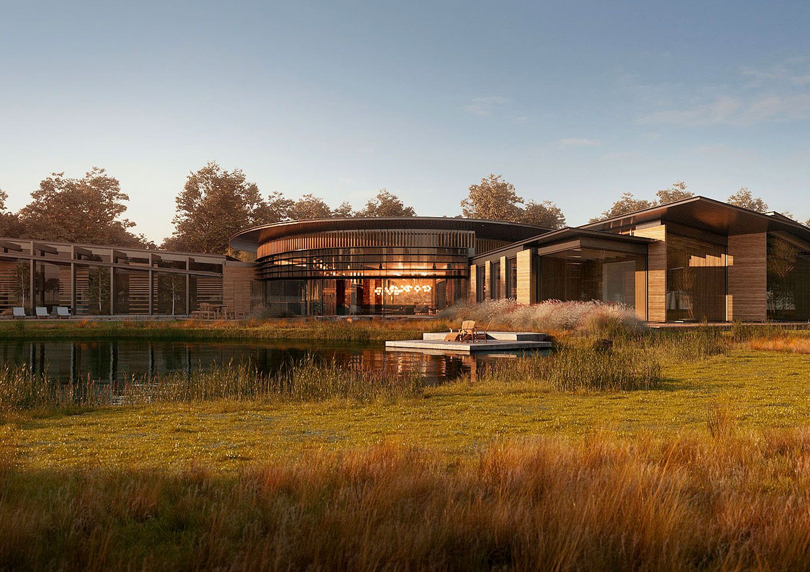 Modern glass-and-wood house by a pond, surrounded by tall grass and trees at sunset.
