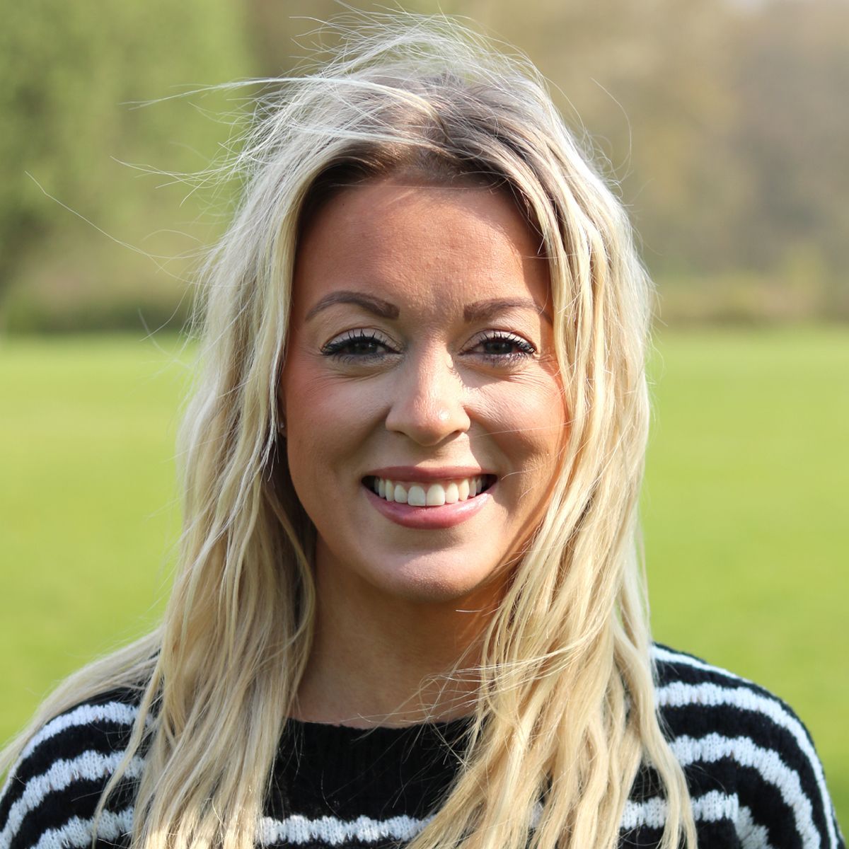 Smiling woman with long blonde hair in a black-and-white striped sweater outdoors