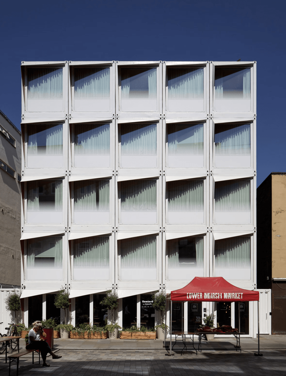 White modern building with geometric windows and a red awning in front under a blue sky