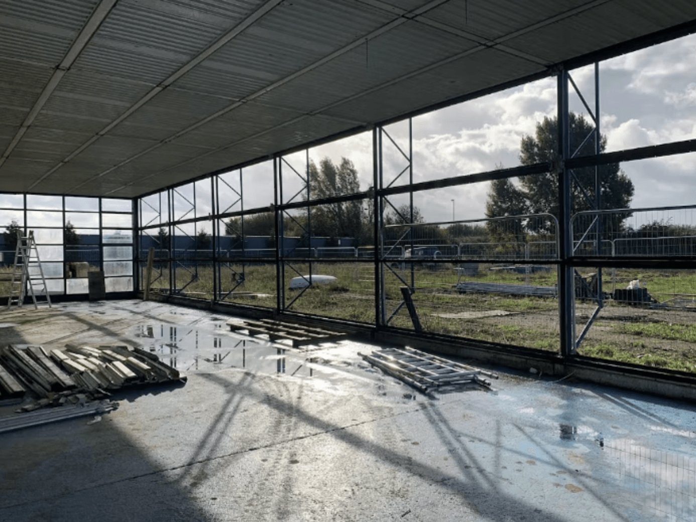 Empty indoor construction site with metal framing, stacked materials, and sunlight streaming through large windows