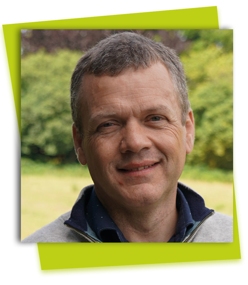 Smiling man in a gray sweater outdoors with a blurred green background