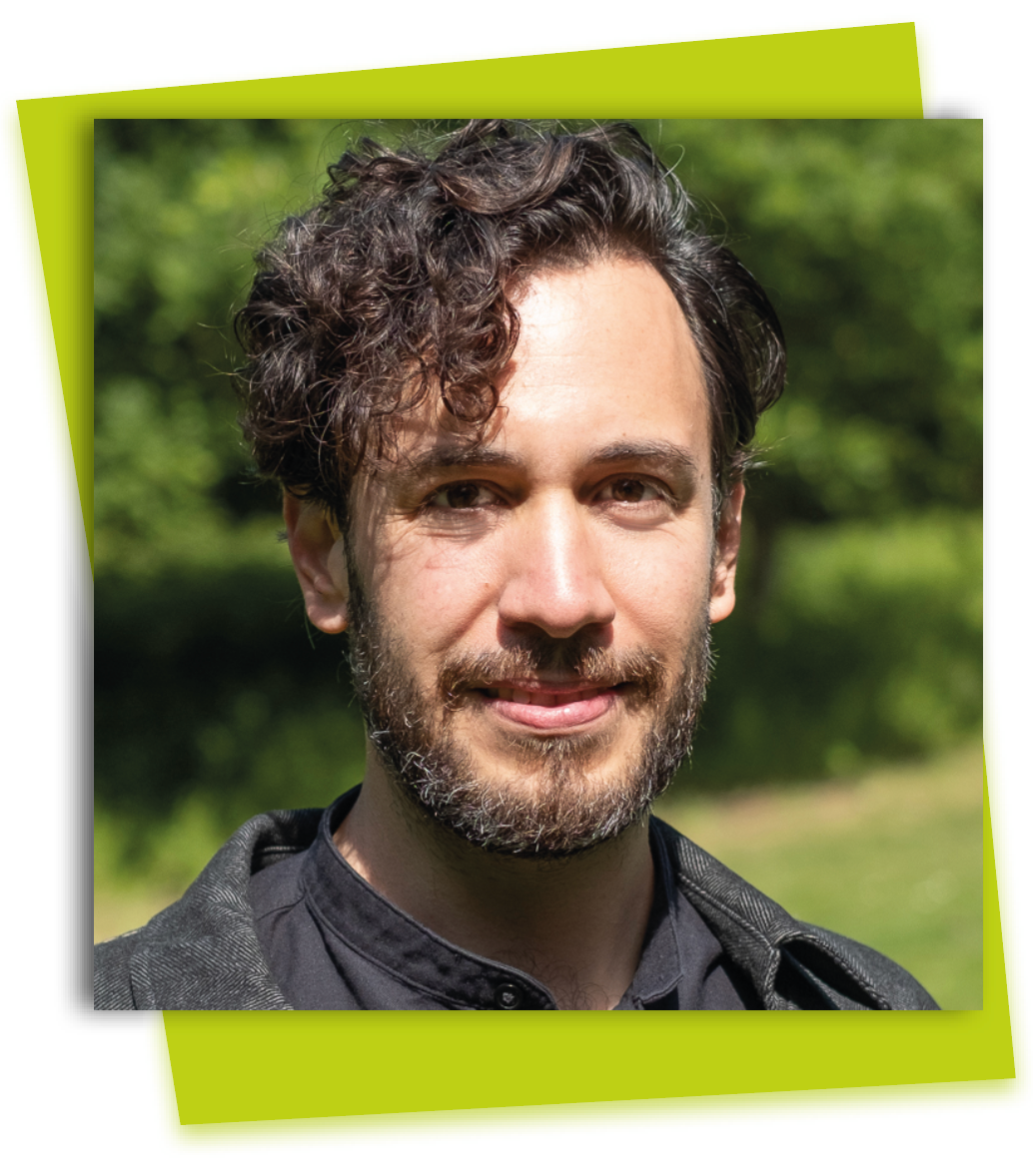 Portrait of a curly-haired person with a slight smile, outdoors against a blurred green background.