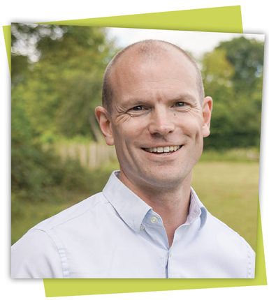 Smiling bald man in a white shirt outdoors, framed against a blurred green background.