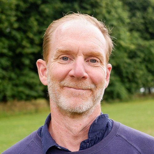Smiling man in a blue jacket standing outdoors in a green park