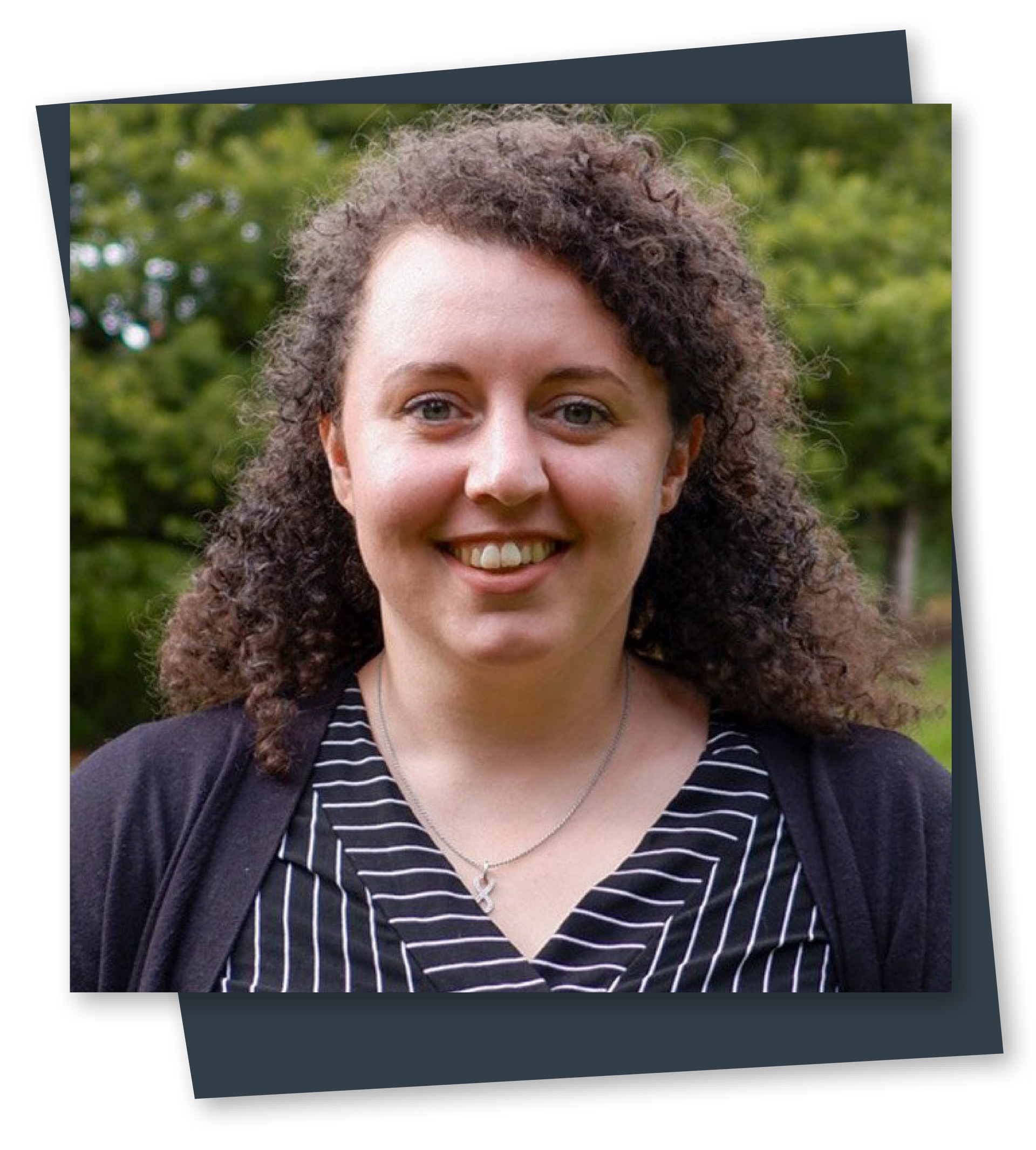 Portrait of a smiling woman outdoors with curly hair, wearing a striped top and dark cardigan.