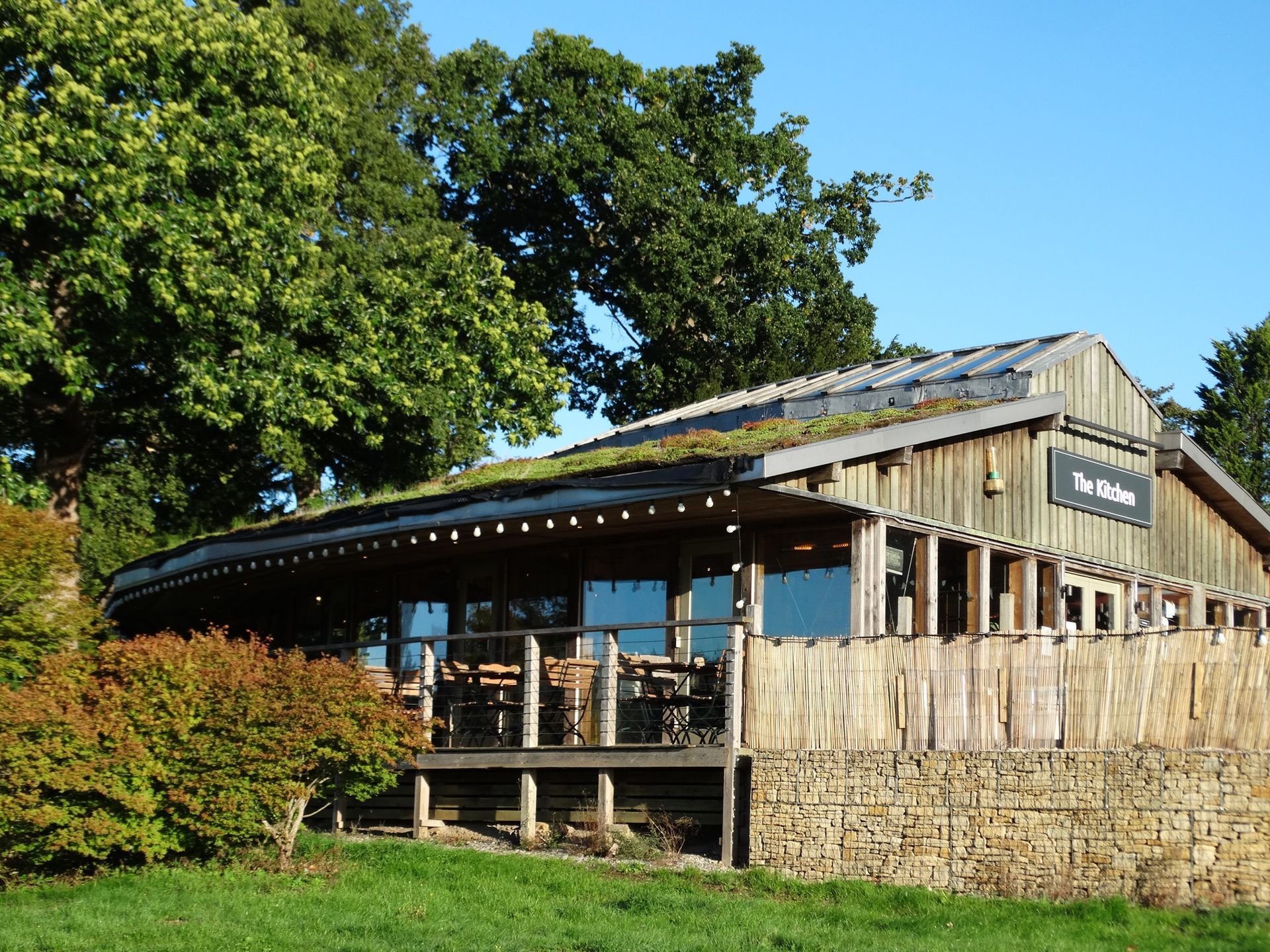 Rustic wooden building with a porch and stone base, surrounded by trees under a clear blue sky.
