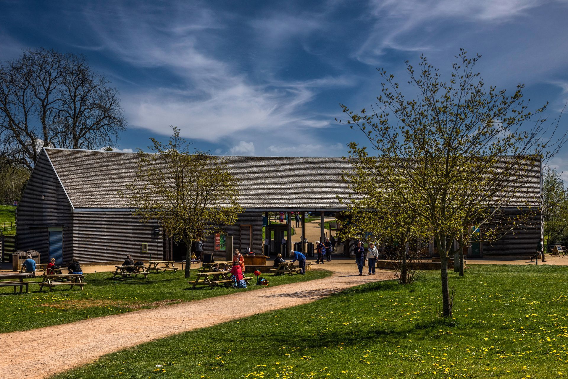 Modern building with striped facade, people outside, and a grassy park under a blue sky