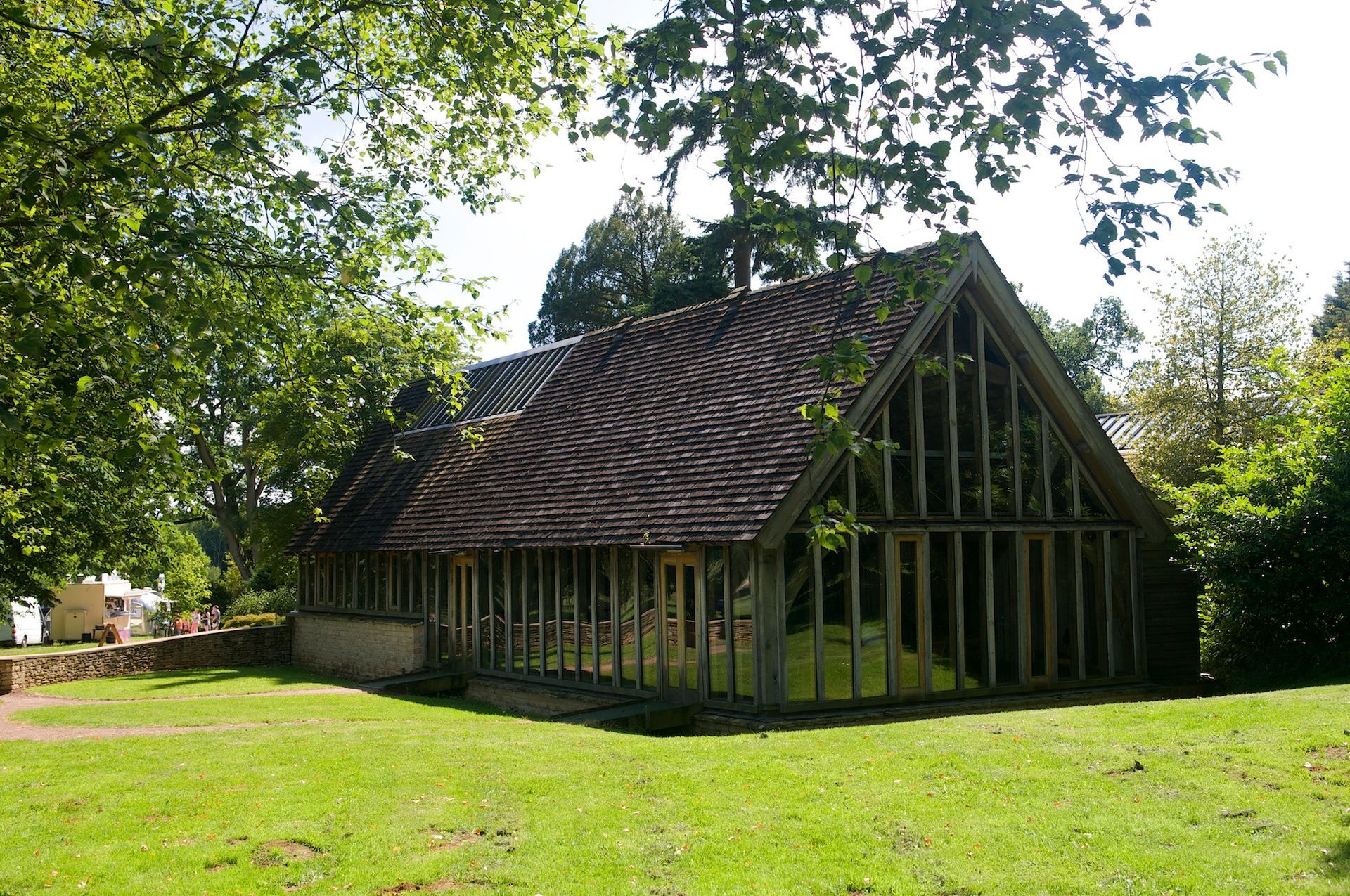 Small wooden cottage with a steep thatched roof in a grassy, tree-lined yard