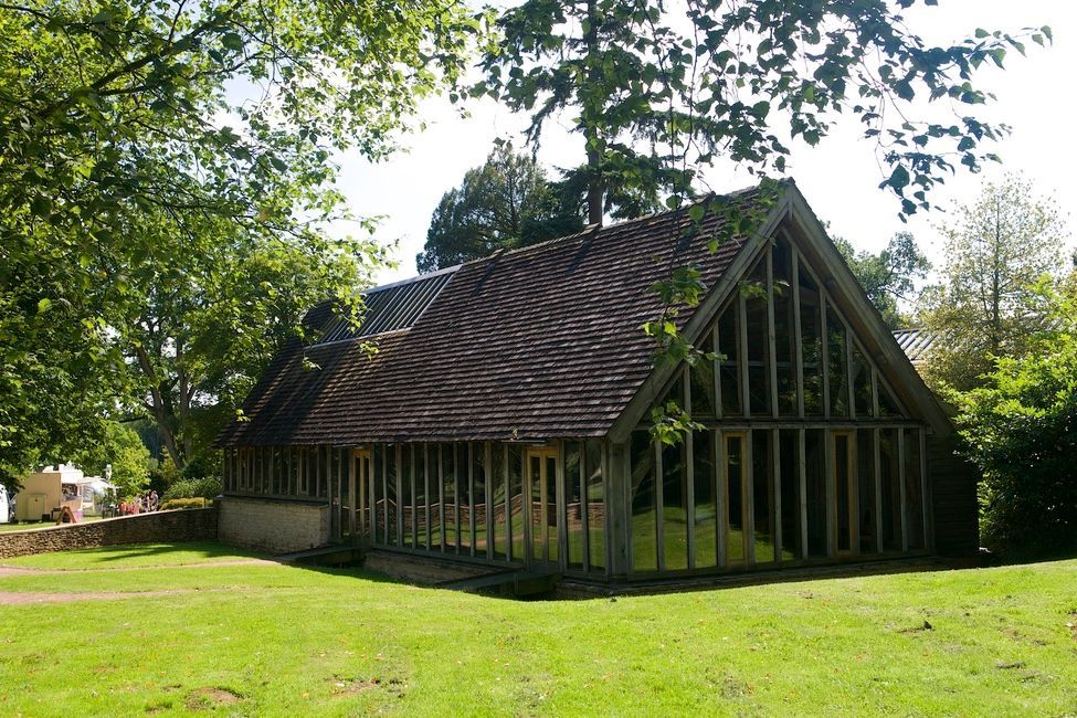 Old timber barn with a steep roof in a grassy clearing under trees