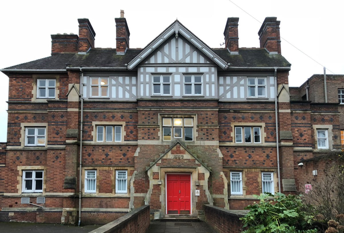 Front view of a brick building with a red door and white-trimmed windows