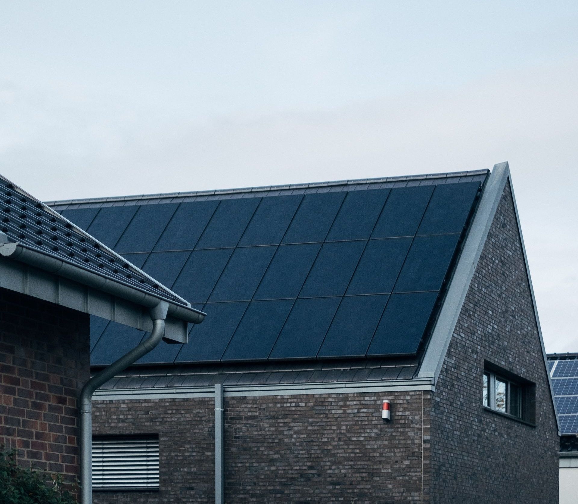 Brick house with dark solar panels on a sloped roof against a cloudy sky