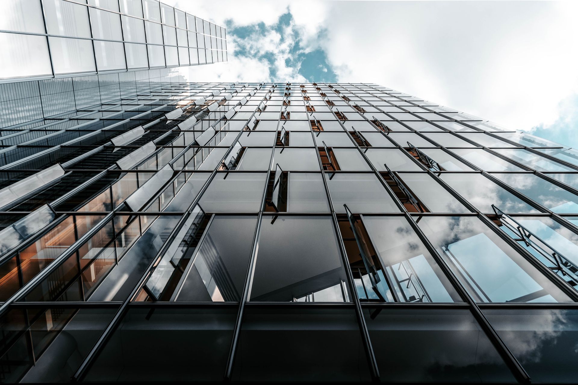 Looking up at a modern glass skyscraper reflecting clouds and the sky