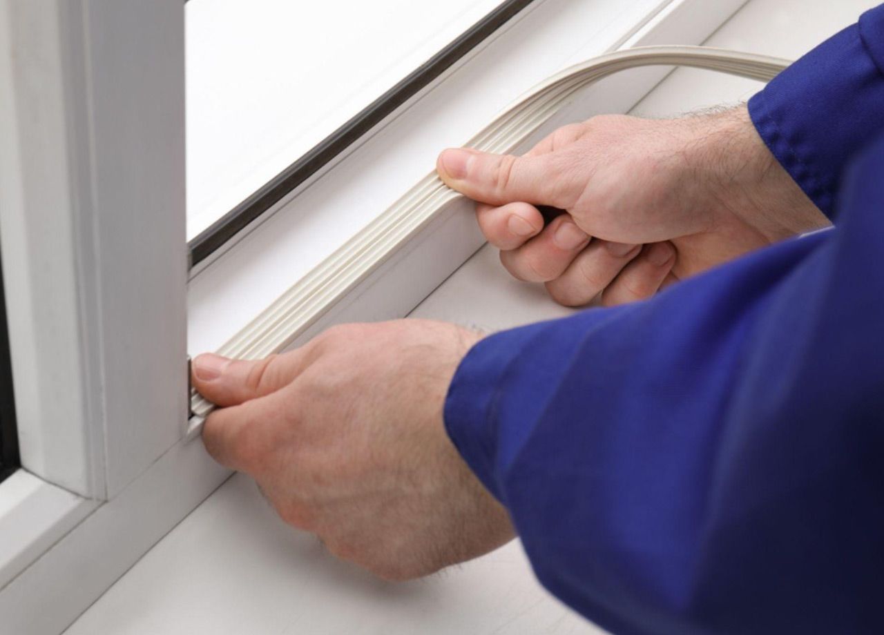 Hands fitting weatherstripping into a window frame with a blue sleeve visible
