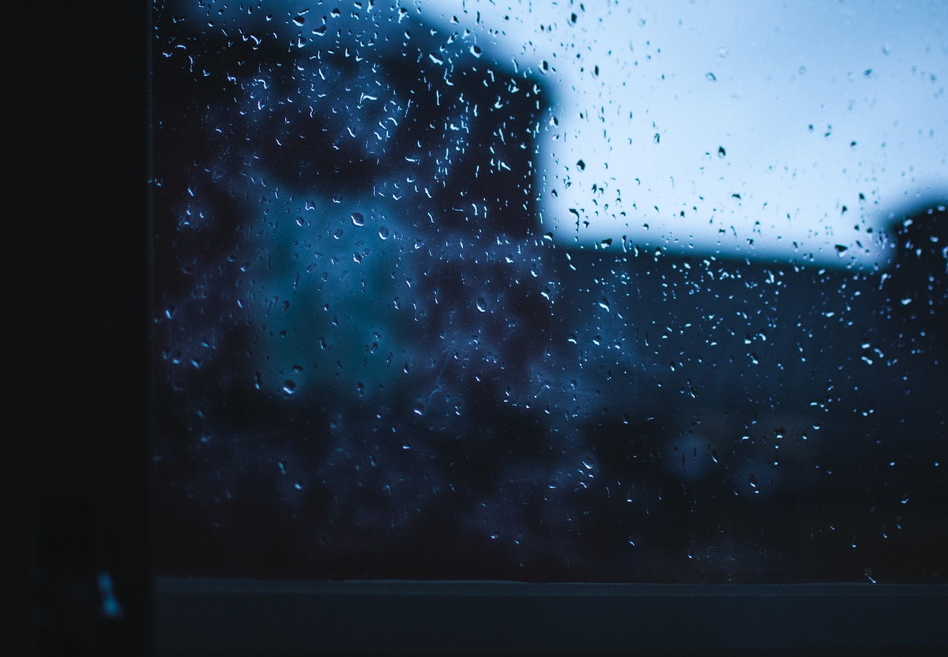 Blue-tinted rain on a window with a blurred person or figure beyond it