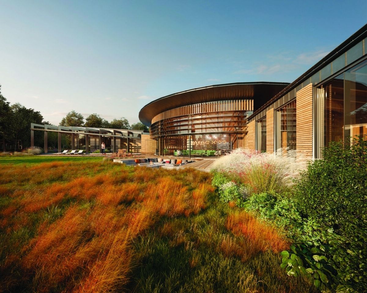 Modern curved building with glass facade beside a landscaped field of orange and green grasses