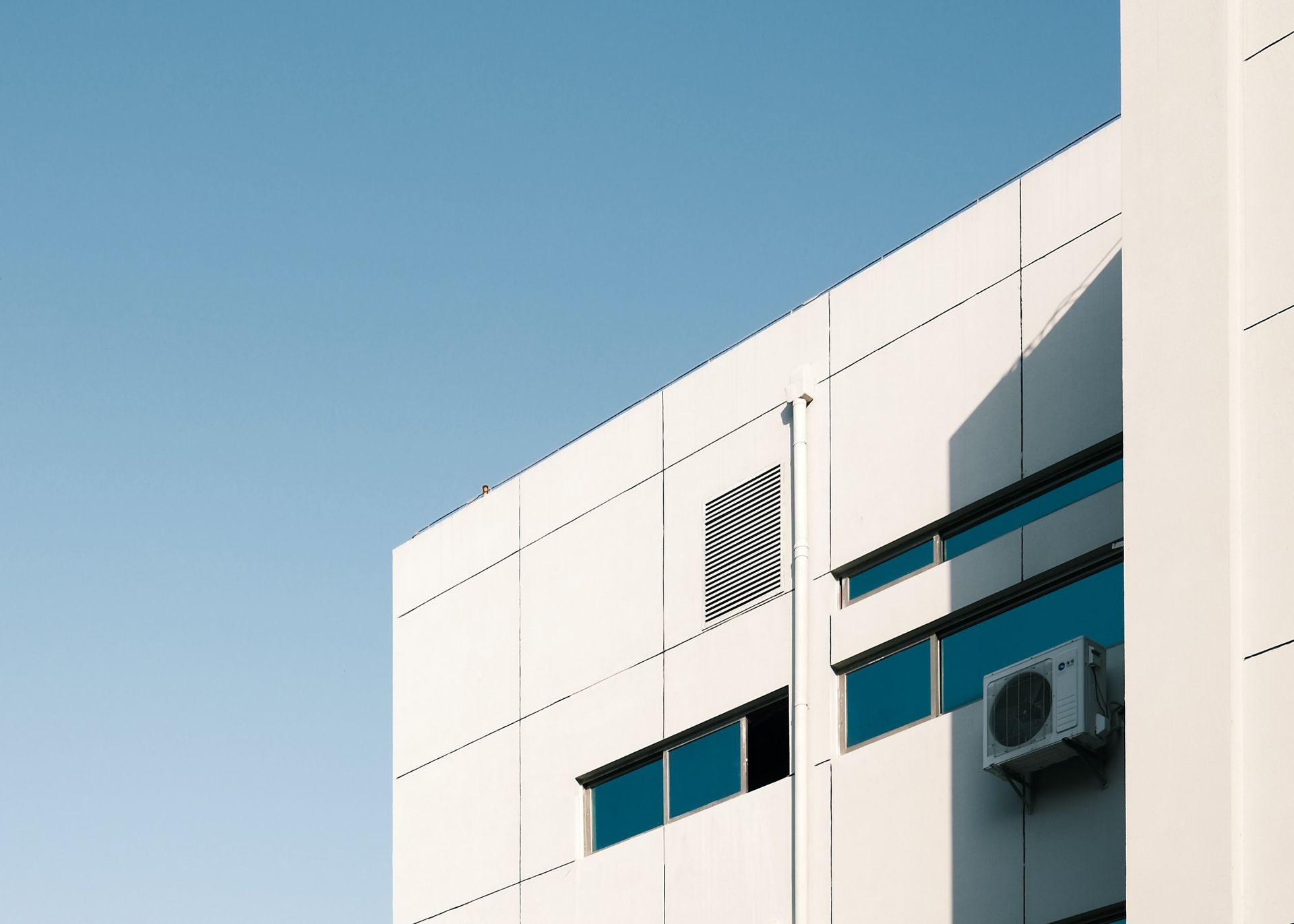 White building facade with blue-tinted windows and an air-conditioning unit against a clear sky