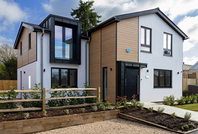 Modern two-story house with white and wood siding, black-framed windows, and a small front garden
