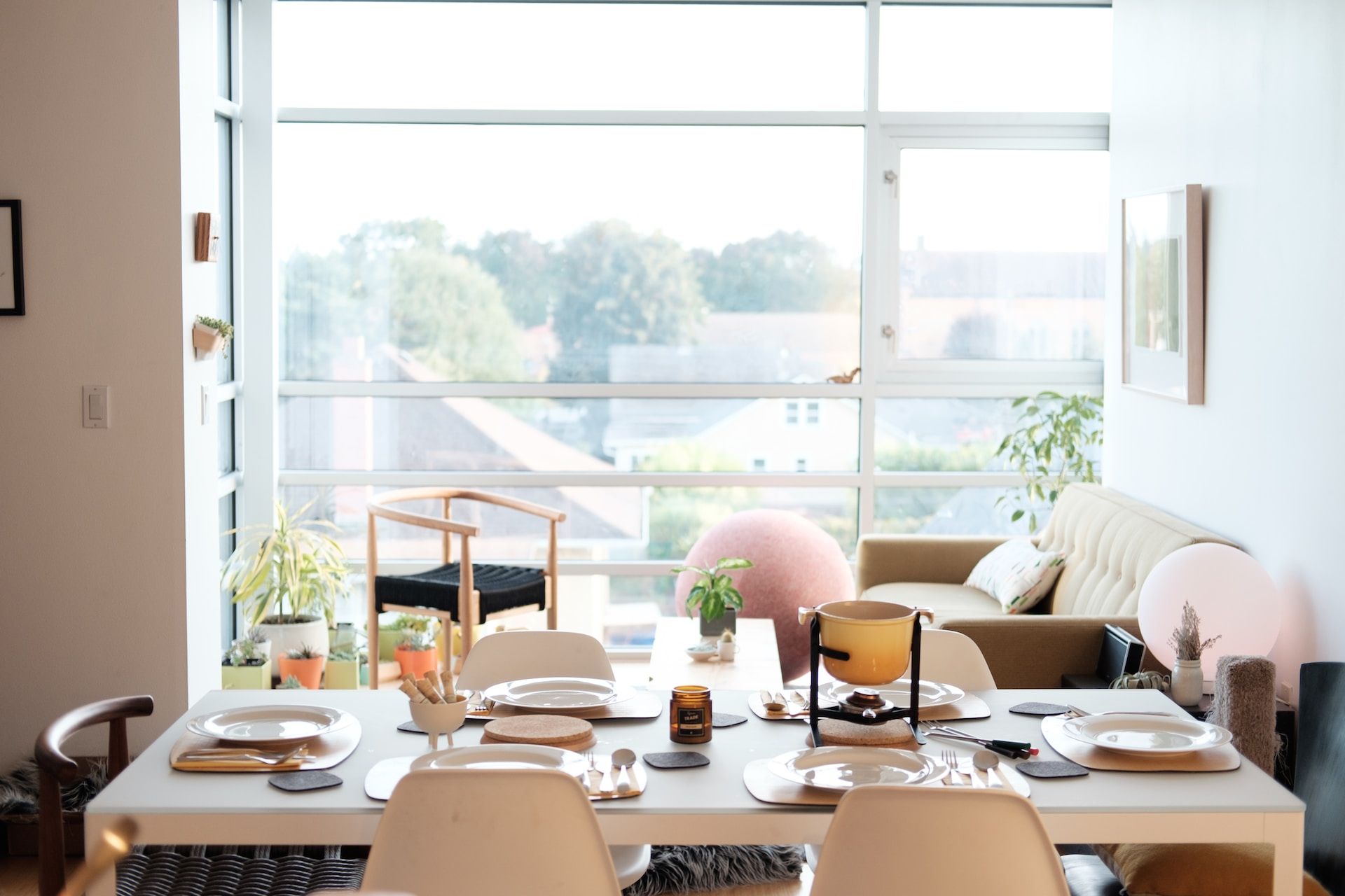 Bright dining room with a set table, large window, and view of a cityscape beyond the balcony.
