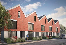 Row of modern red-brick townhouses with angular roofs and a person walking on the sidewalk