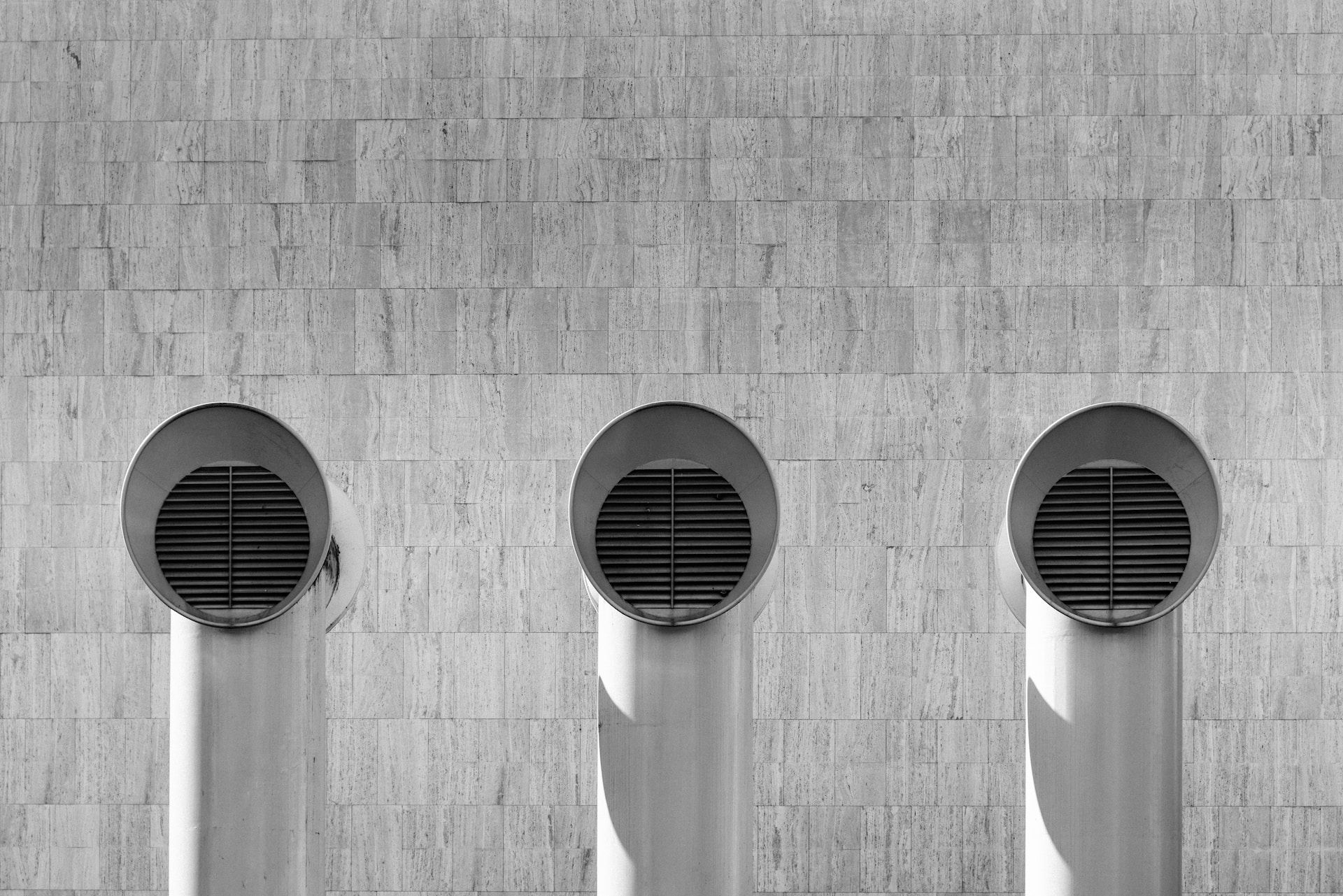 Three round black vents on a gray concrete wall, each casting a long shadow downward.