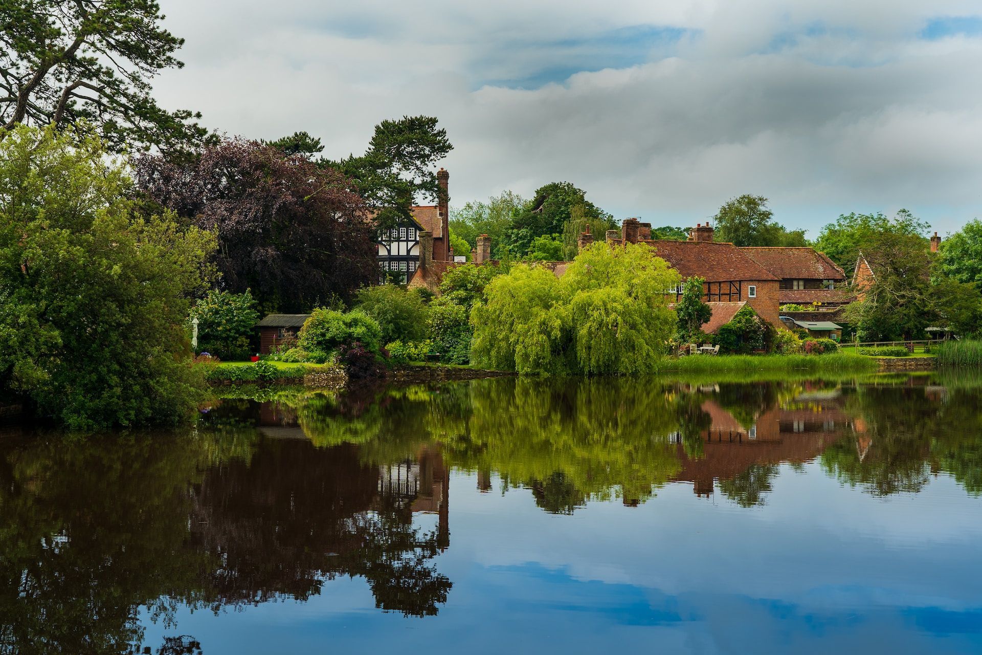 Calm lake reflecting trees and houses under a cloudy sky