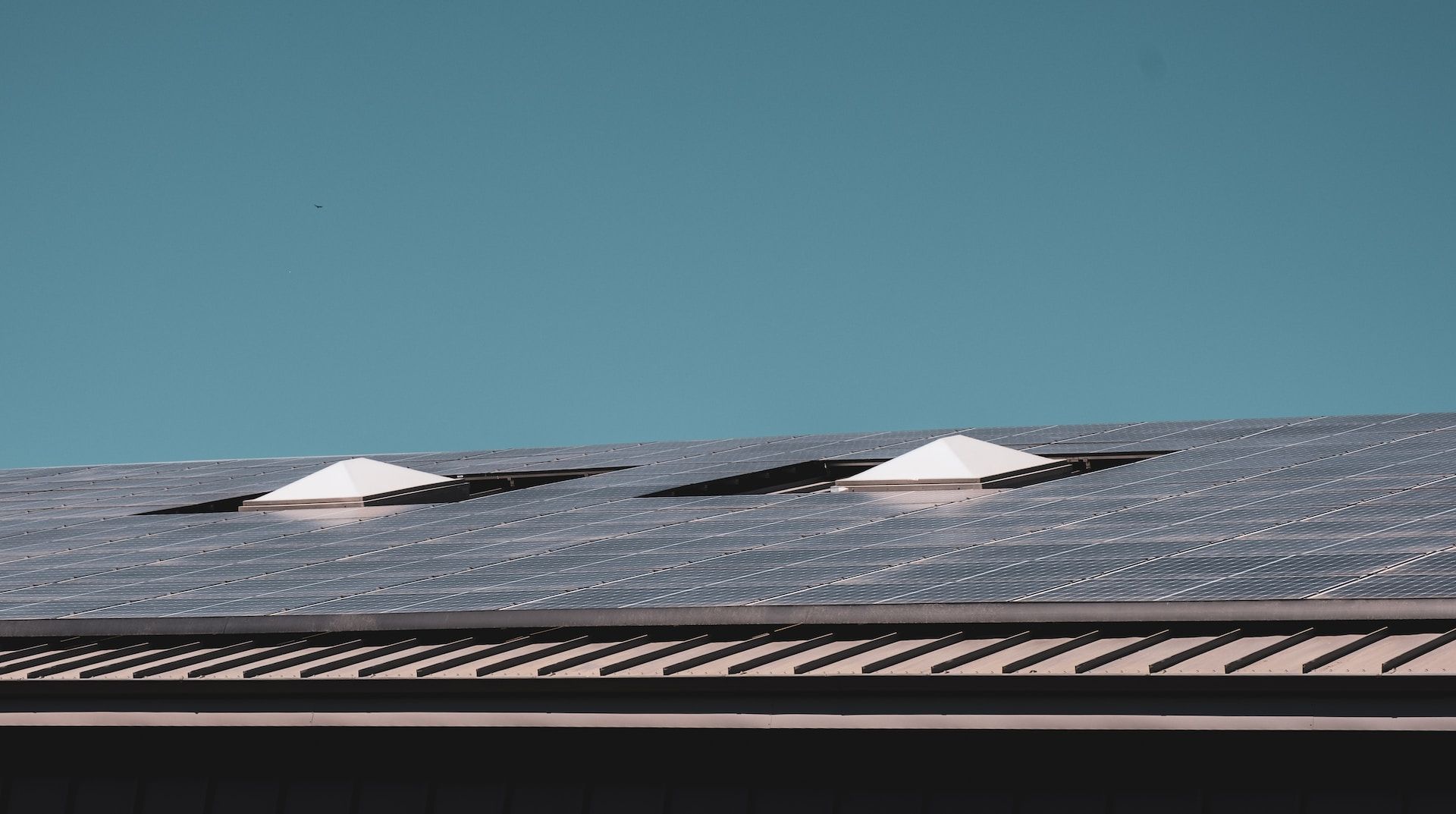Solar panels on a rooftop under a clear blue sky, with patches of snow on top.