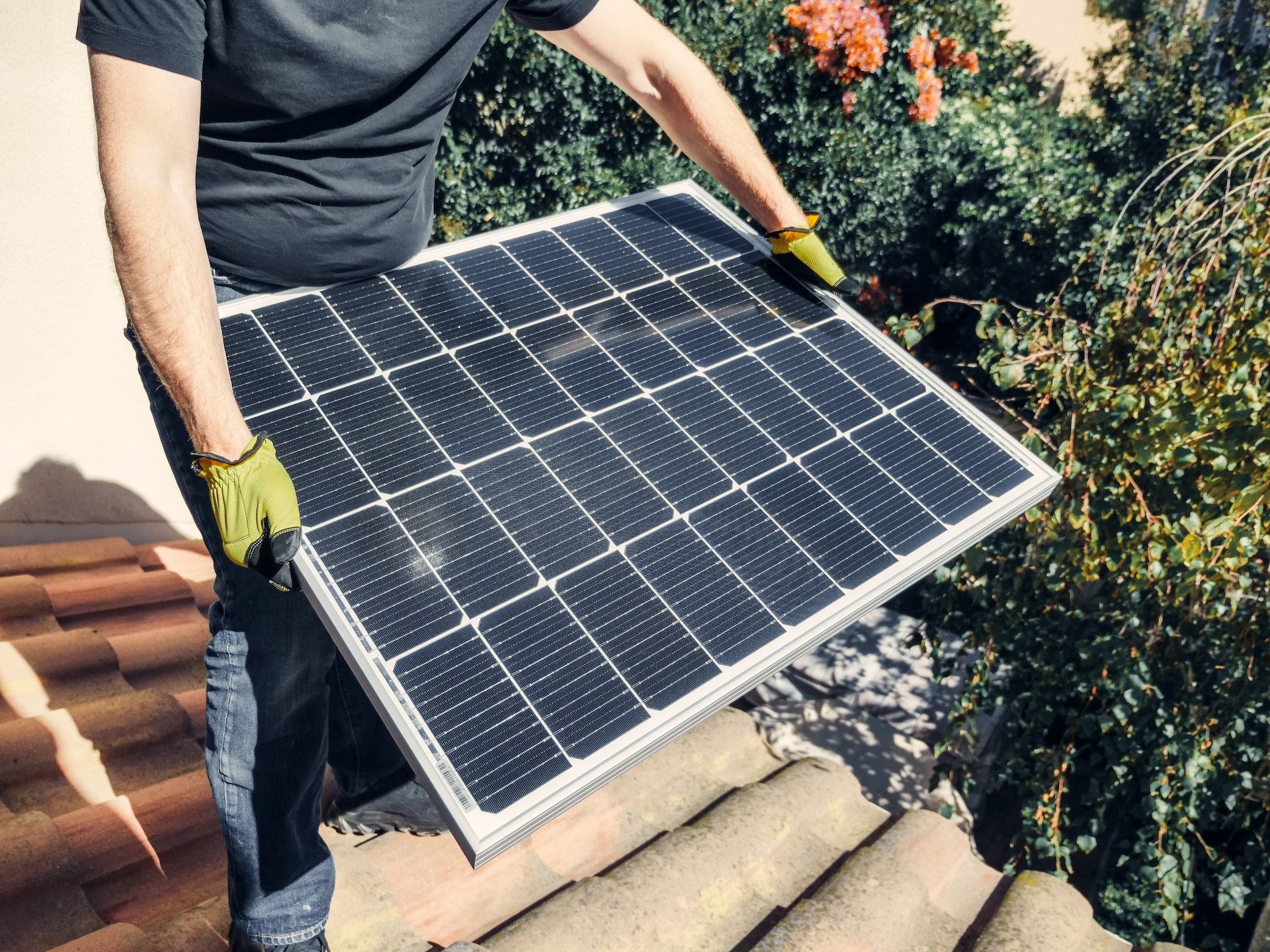 Person wearing gloves carrying a solar panel on a rooftop.