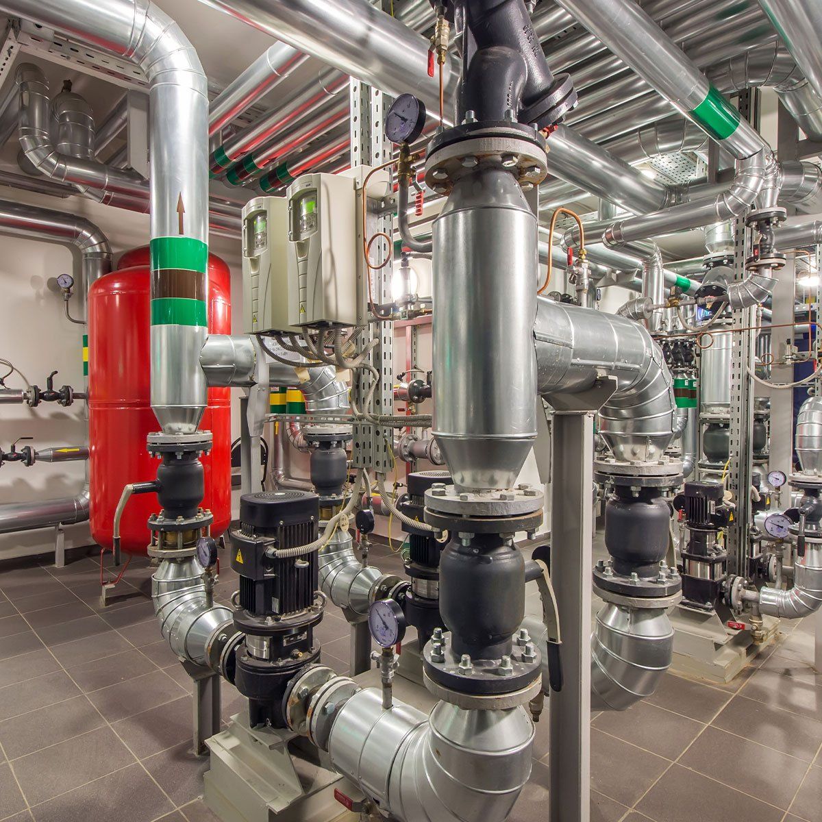 Industrial plant room with shiny silver pipes, valves, and large red machinery.