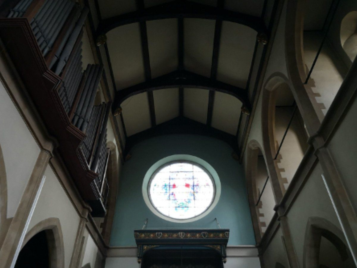 Interior of a church, looking up at arched walls and ceiling toward a round stained-glass window.
