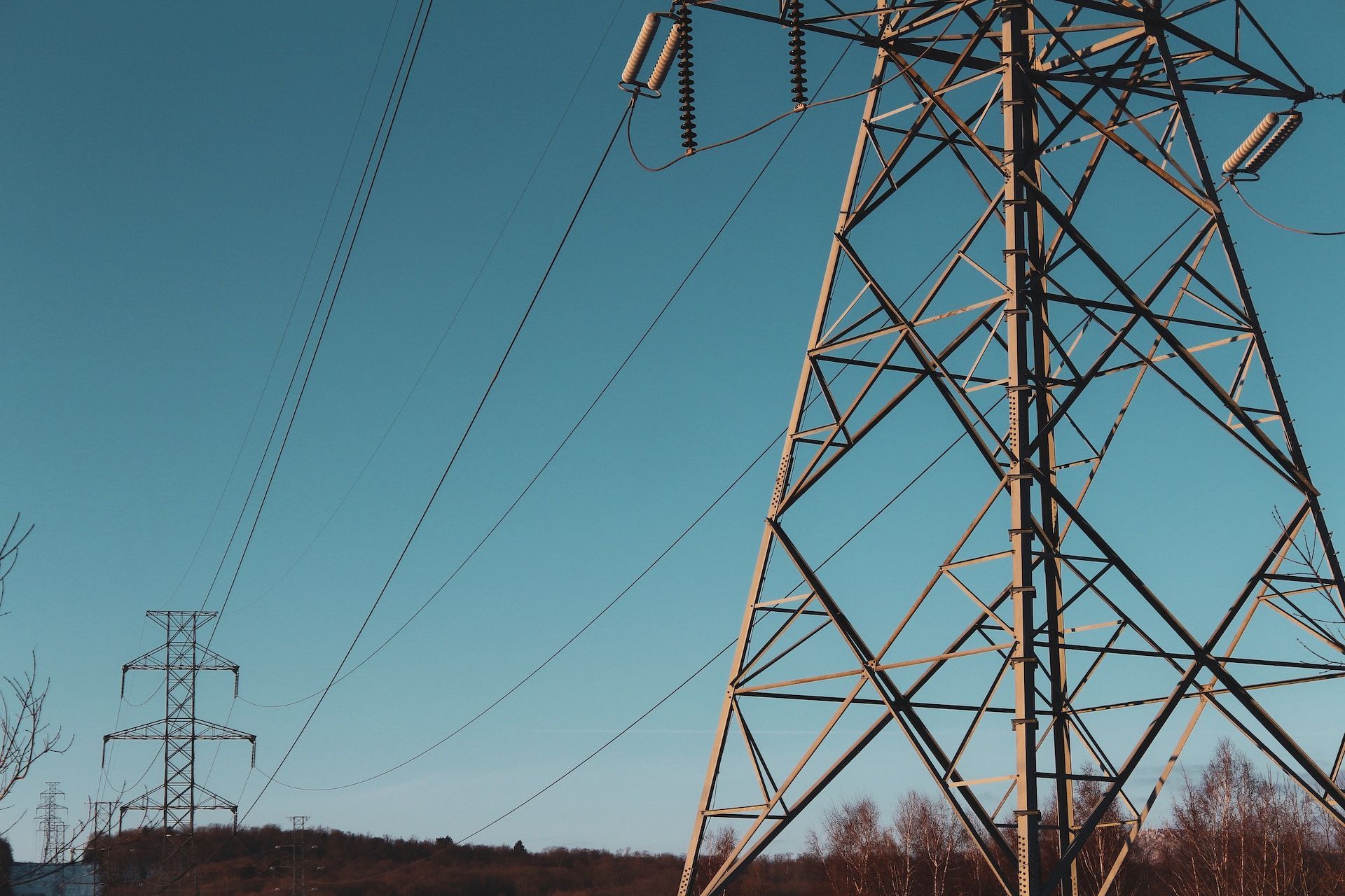 Power lines and steel transmission towers against a clear blue sky