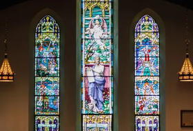 Three stained-glass church windows with colorful biblical figures and hanging lanterns on either side