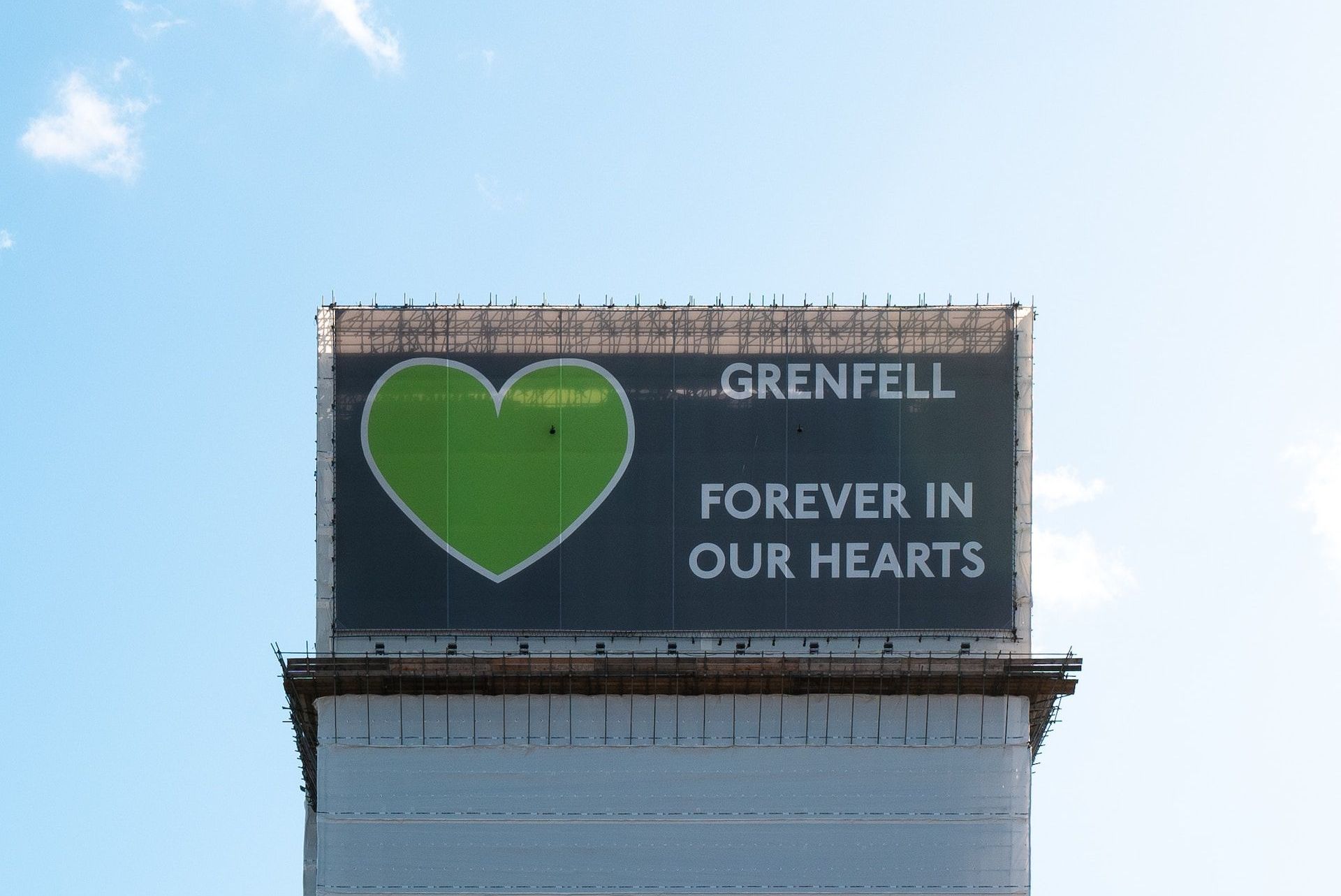Grenfell Tower memorial sign with a green heart and “Forever in our hearts” text