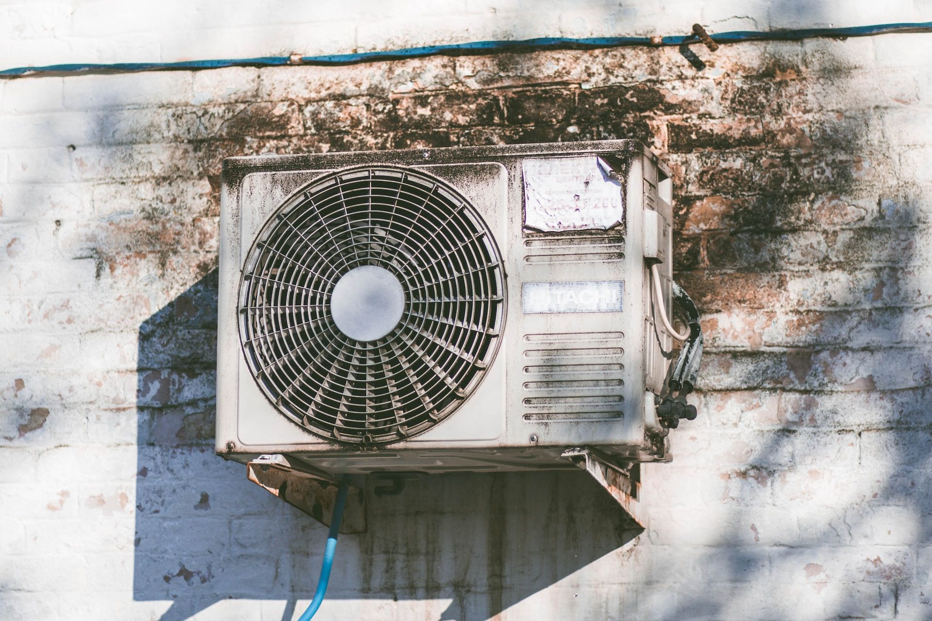 Wall-mounted outdoor air conditioner unit on a weathered stucco wall with shadows.