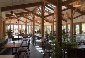 Rustic restaurant dining room with wooden beams, large windows, tables, and hanging pendant lights